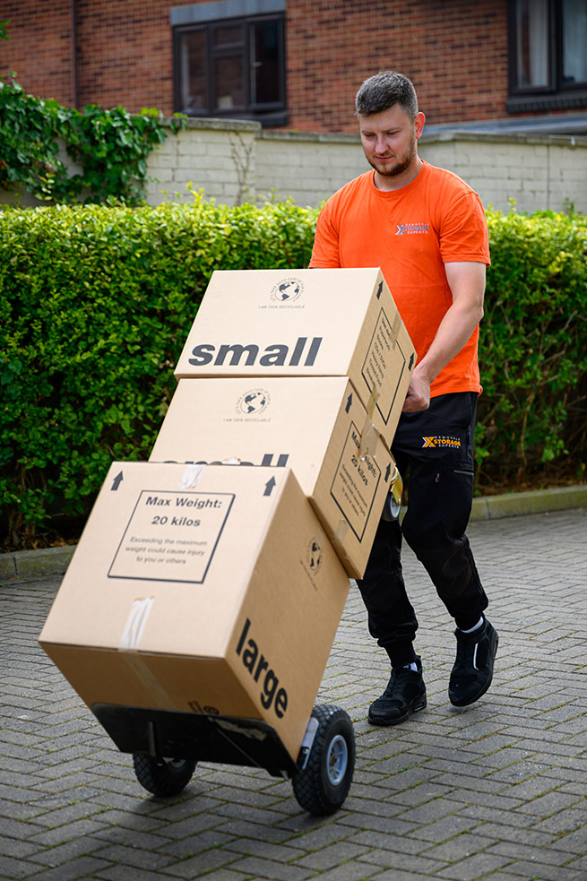 Two workers carry storage bins with pink lids outside a building.