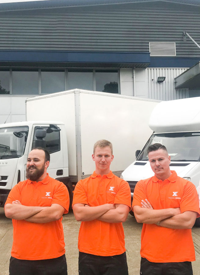 Three "Removals & StorageX" workers stand with arms crossed in front of removal trucks.