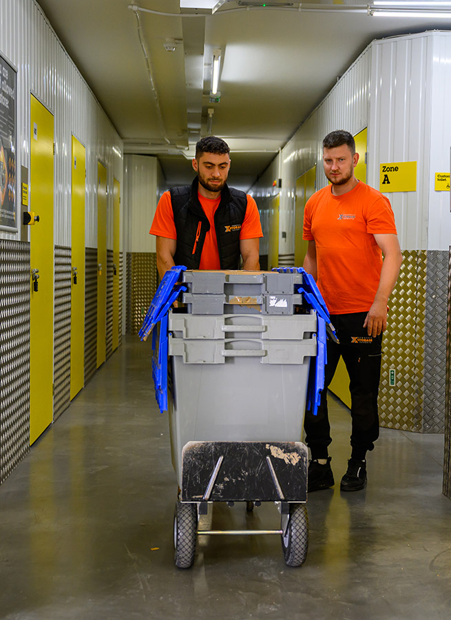 Workers load crates from a truck on a busy city street, with a branded truck visible.